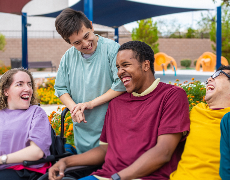 A stock photo of some young disabled people sharing a joke on an outside terrace.