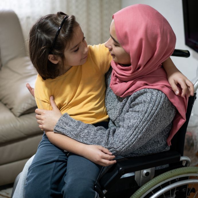 An image of a woman in a wheelchair with a young girl sitting on her knee (c) Carers Trust